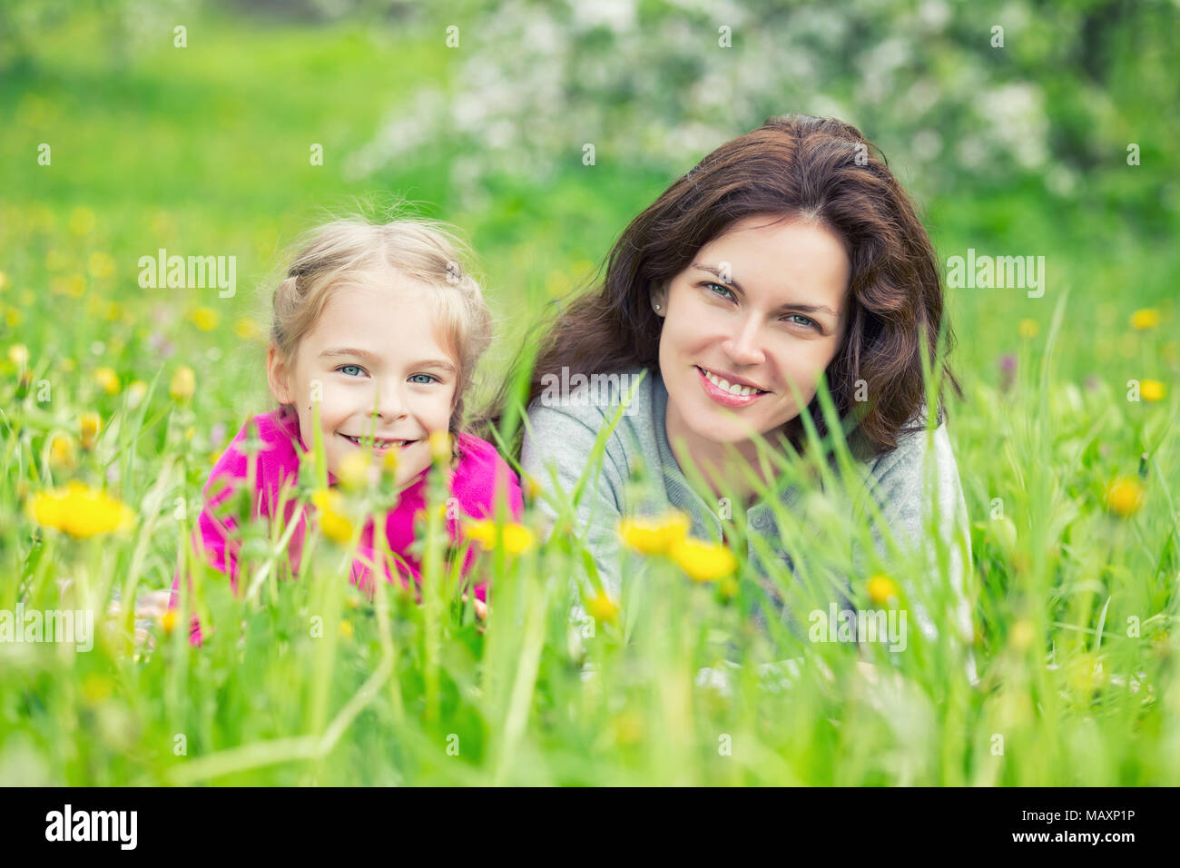 Mutter und Tochter liegen auf grüner Sommer Gras mit blühenden gelben Blumen Stockfoto