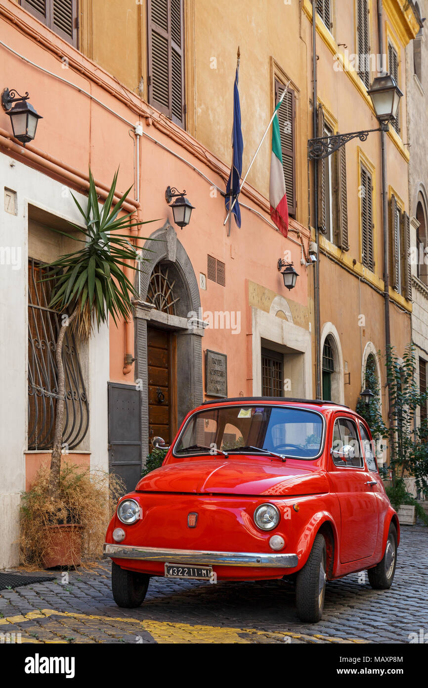Eine ikonische alten roten Fiat 500 in einer gepflasterten Straße in Rom, Italien, außerhalb eines Gebäudes unter italienischer Flagge geparkt. Stockfoto