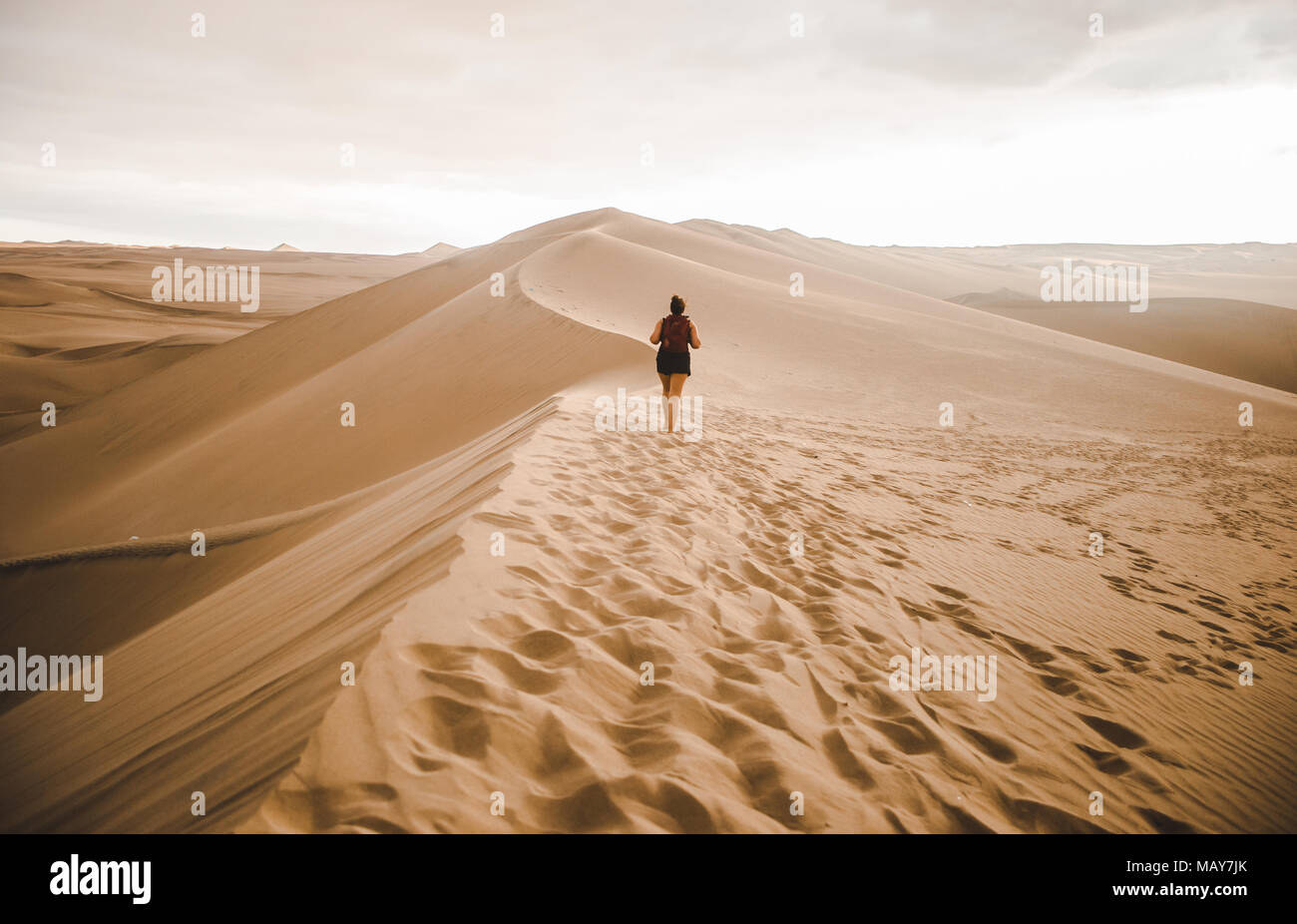 Junge tausendjährigen Frau tourist/Reisenden geht über eine Sanddüne in der Wüste mit einem roten Rucksack in Huacachina, Peru Stockfoto