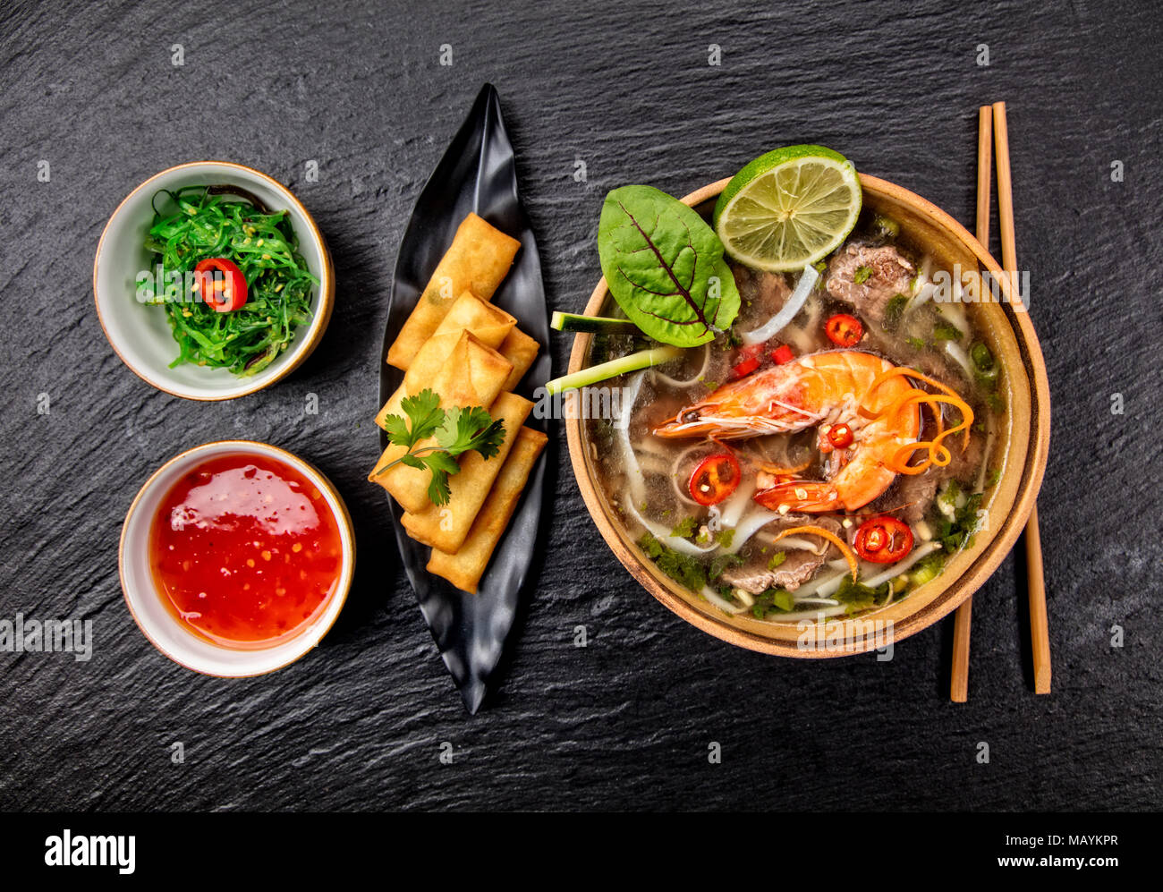 Asiatische Garnelen Suppe mit Frühlingsrollen und Stäbchen. Ansicht von oben, auf schwarzen Stein serviert. Stockfoto