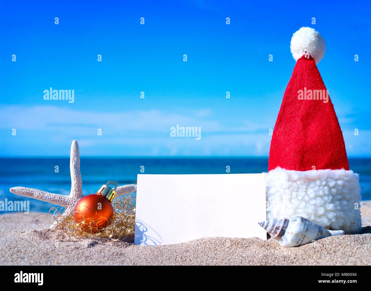 Weihnachten Grußkarte und Weihnachten Dekoration am Strand. Strand Szene mit Seesterne, Muscheln und Sand. Christmas tree Ball und leeren weißen Karte. Stockfoto