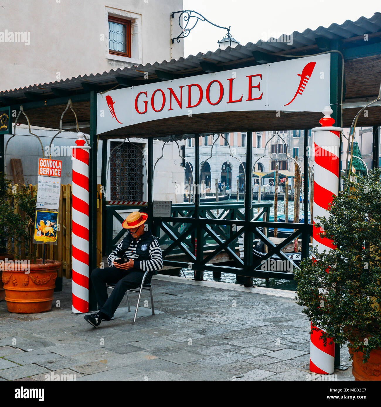 Gondoliere entspannt neben einem Schild mit dem traditionellen roten und weißen Stöcke Werbung Gondel Dienstleistungen Stockfoto