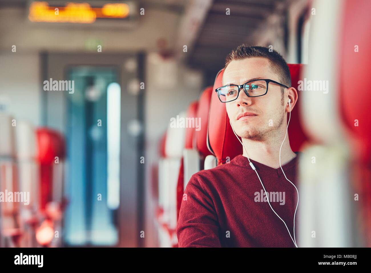 Transport auf der Schiene. Nachdenklichen jungen Mann mit Brille Musik hören, während Sie mit dem Zug. Stockfoto