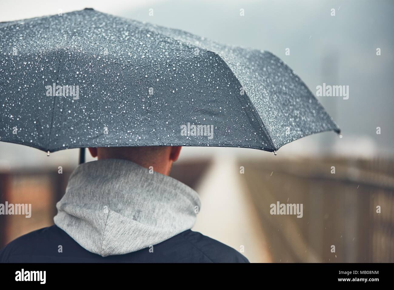 Mann mit Schirm im Regen. Düstere Wetter in der Stadt. Selektiver Fokus auf die Regentropfen. Stockfoto