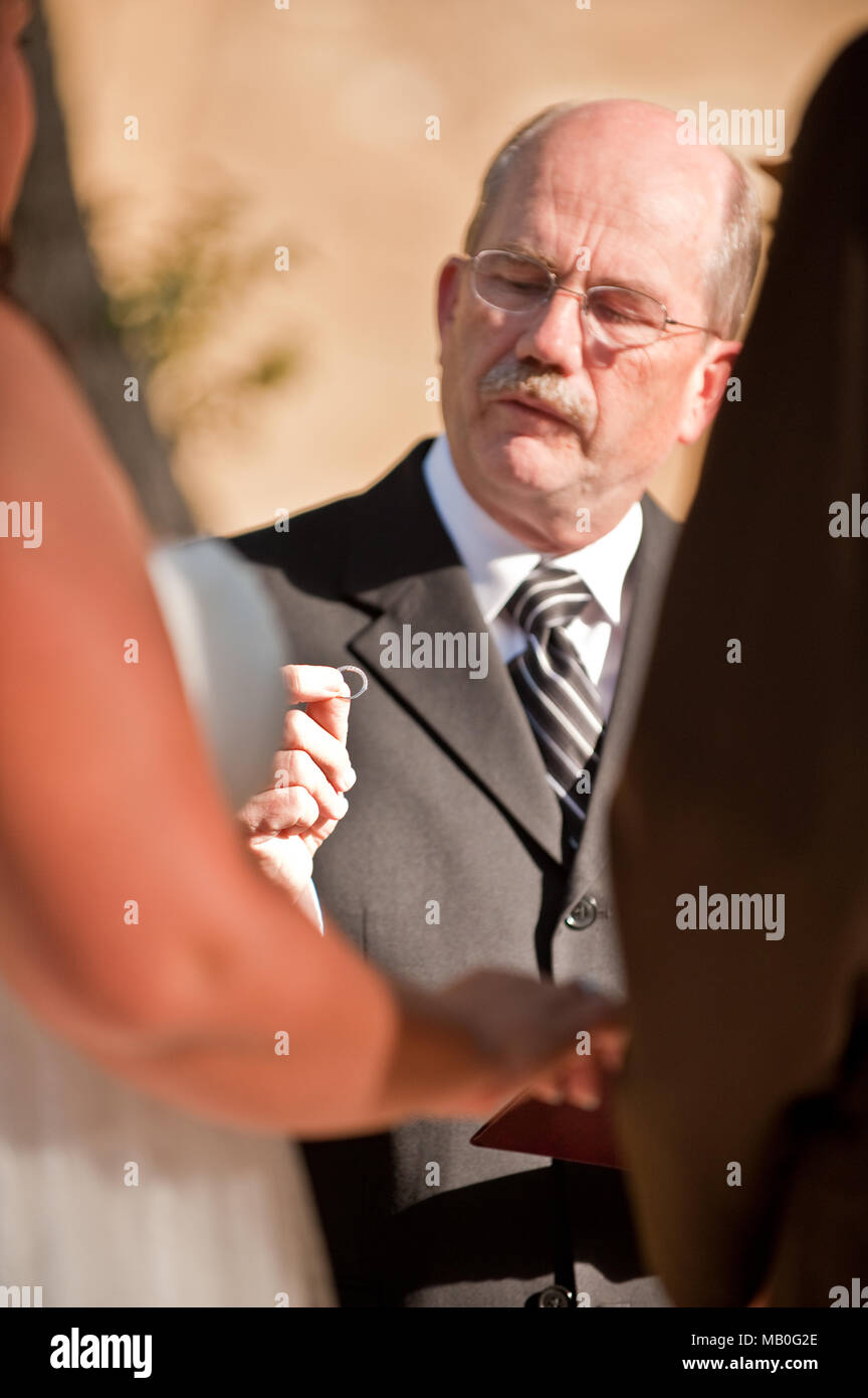 Ein Priester amtiert eine Hochzeit mit einem Hochzeit Ring in der Hand vor der Braut und des Bräutigams, die jede andere Hände an einer im Hochzeit halten Stockfoto