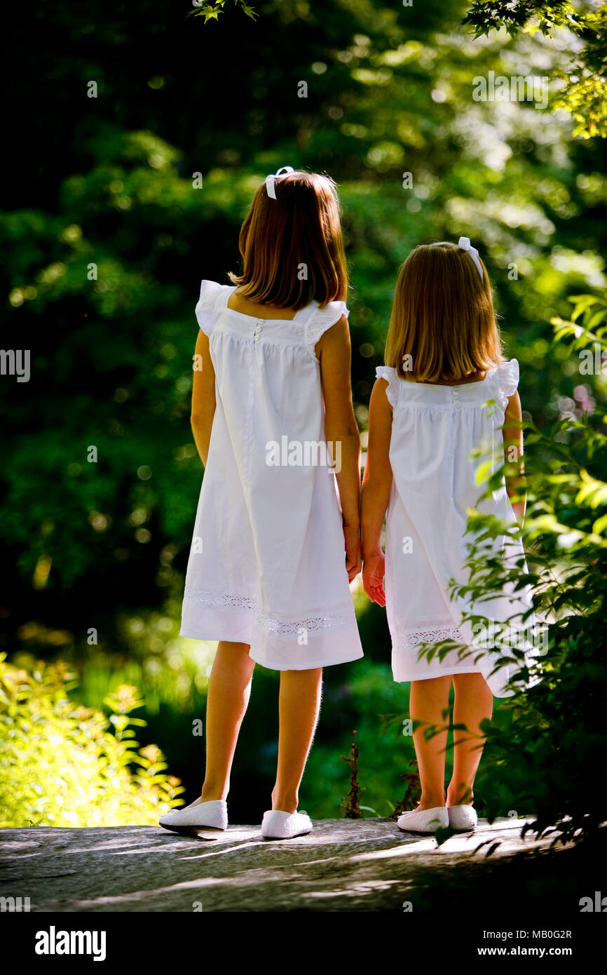Zwei junge Mädchen Caucansian in passende weiße Röcke und weiße Schuhe halten Hände weg von der Kamera an einem sonnigen Park posing Stockfoto