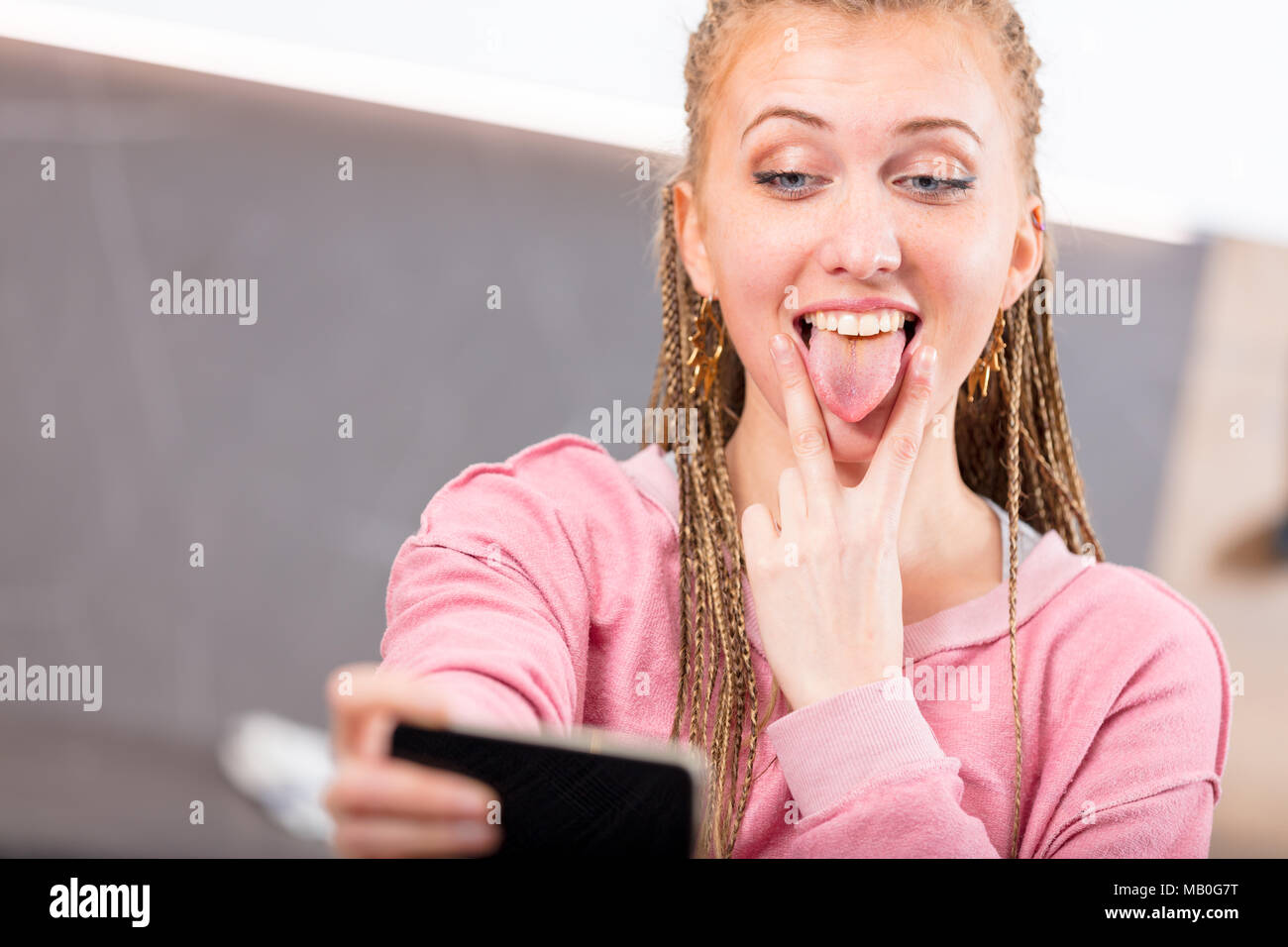 Spaß junge Frau zog ein goofy Gesicht heraus Ihre Zunge und ein V-Zeichen, da sie nimmt ein selfie auf Ihrem Mobiltelefon Stockfoto