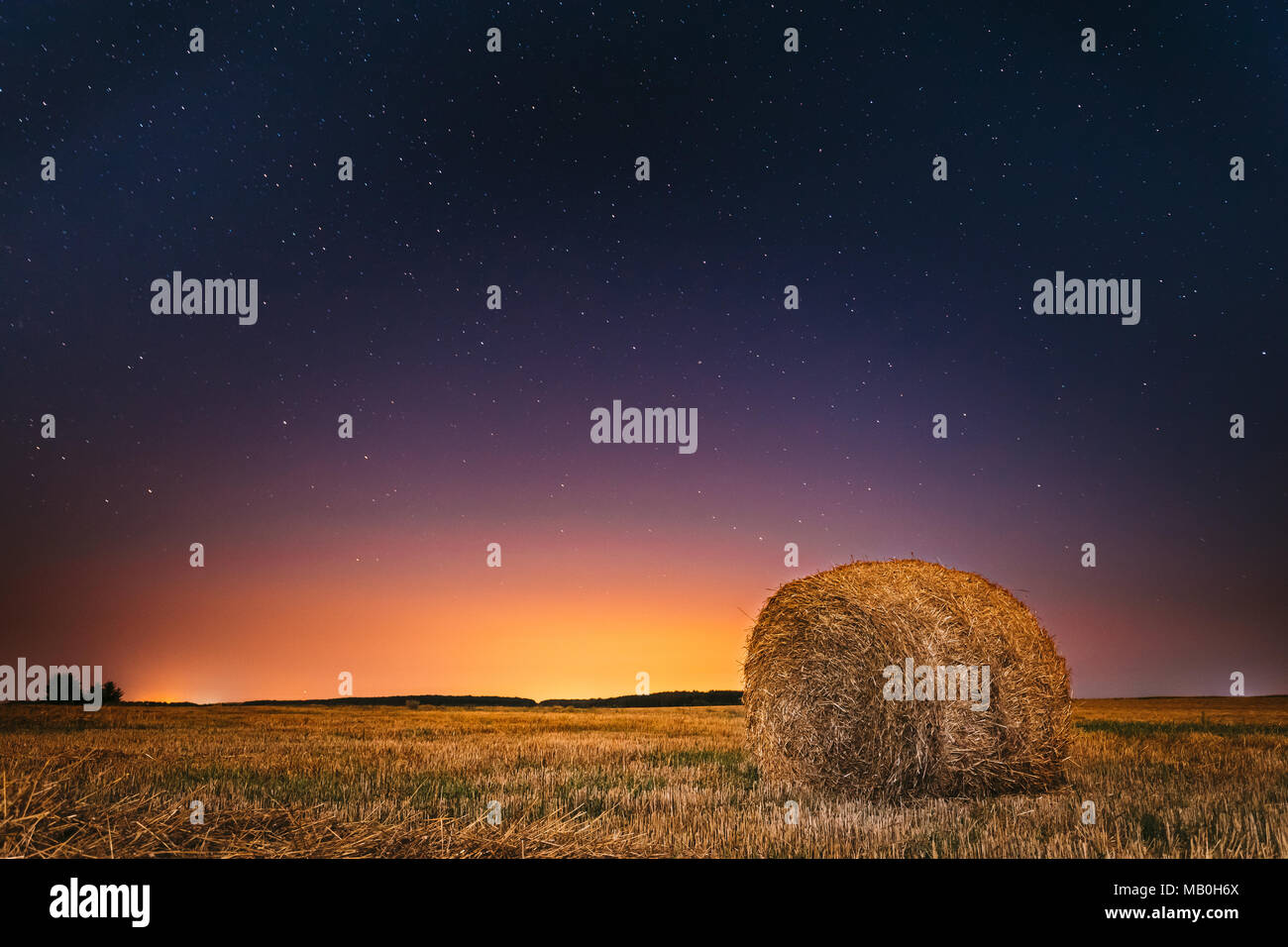 Natürliche Nacht Sternenhimmel über dem Feld Wiese mit Heu Ballen nach der Ernte. Leuchtende Sterne und Sonnenuntergang Sonnenaufgang Anzeigen oberhalb der ländlichen Landschaft im August Monat Stockfoto