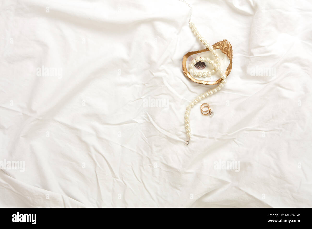 Gold oyster Schmuck Gericht mit Perlenkette und gold Engagement Ring und gold Hochzeit Band auf einem weißen Stoff Hintergrund Stockfoto