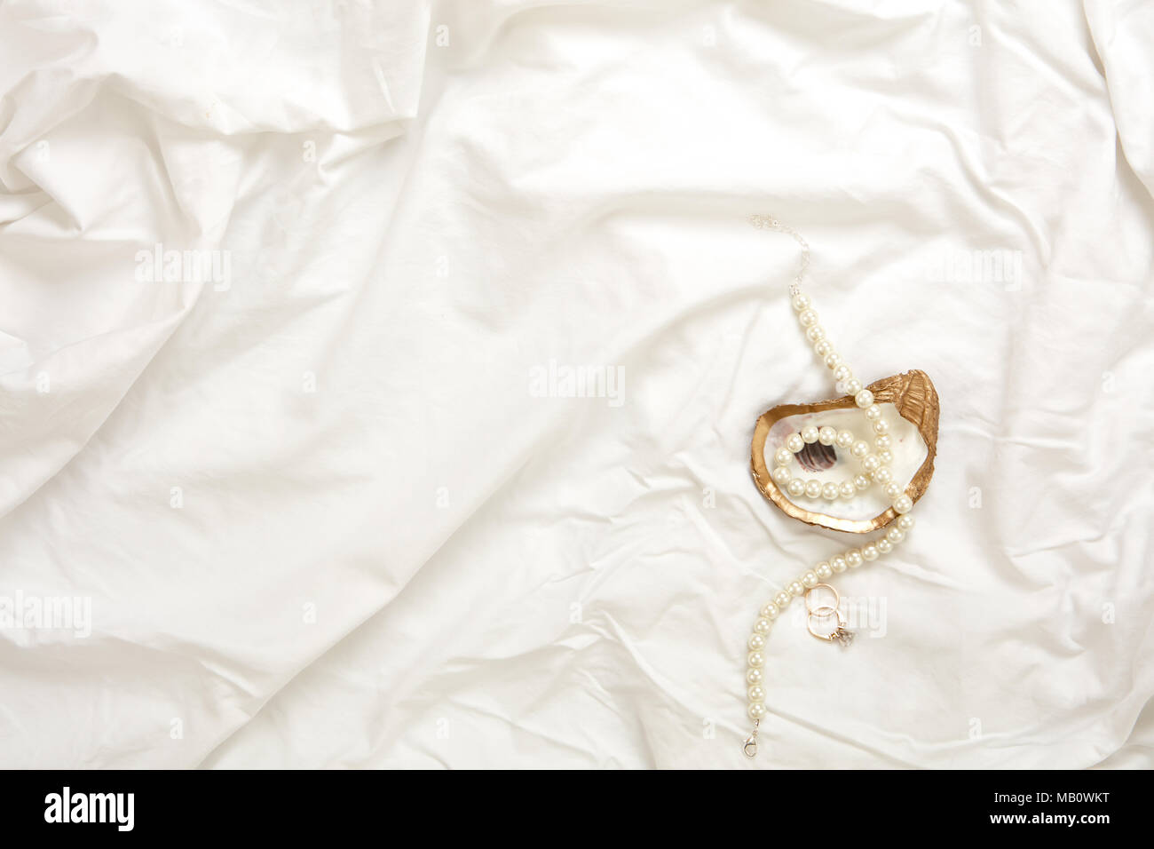 Gold oyster Schmuck Gericht mit Perlenkette und gold Engagement Ring und gold Hochzeit Band auf einem weißen Stoff Hintergrund Stockfoto