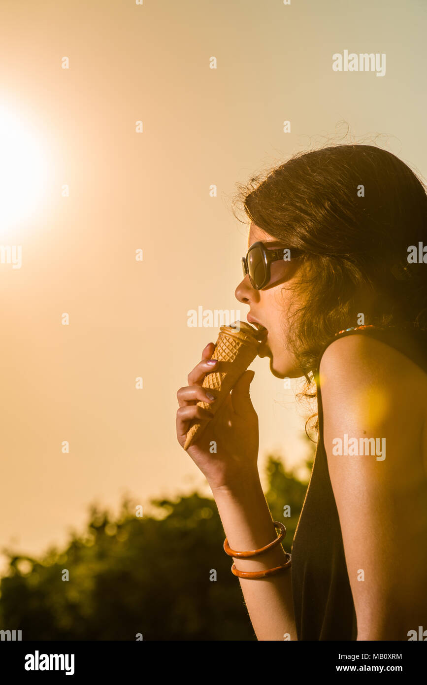 Junge und attraktive Frau Eis essen im Grünen bei Sonnenuntergang Sonnenbrille tragen Stockfoto