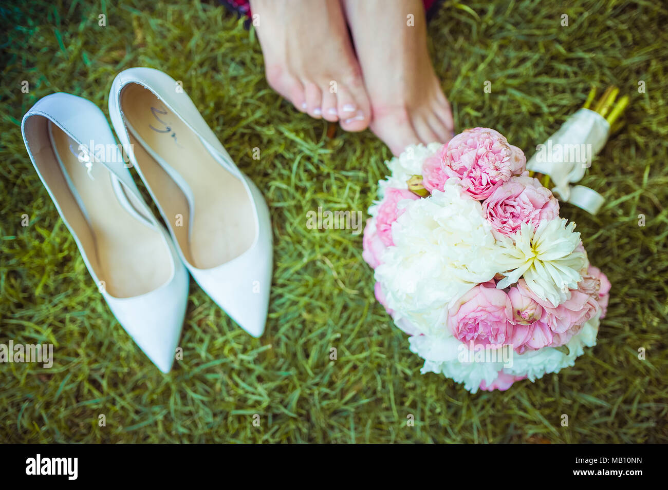 Woman's tragen, die Füße auf dem Gras mit Pfingstrose Bouquet und weißen High Heels neben Stockfoto