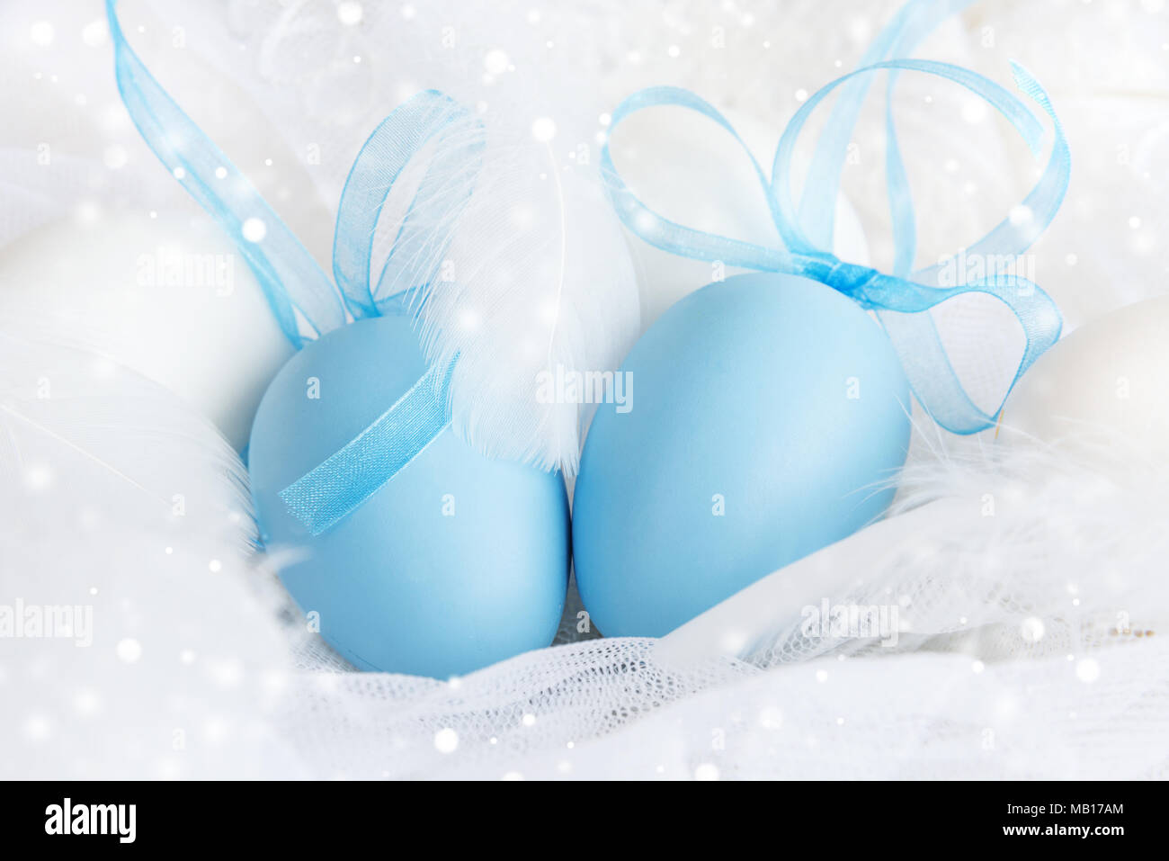 Blaue Ostereier mit blauen Bändern durch weiße Ostern Eier und flauschigen weißen Federn auf einer Schnur weißen Hintergrund umgeben Stockfoto