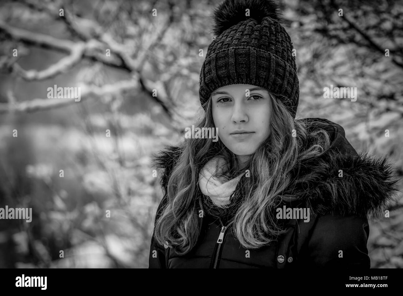 Closeup Portrait von recht jugendlich Mädchen im Winter, Schwarz und Weiß. Schönen kaukasischen Jugendmädchen in schwarzen Mantel, verschwommenes verschneiten Wald im Hintergrund. Stockfoto