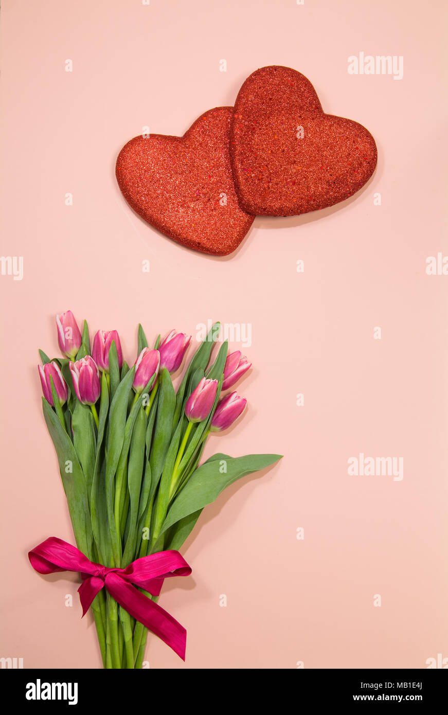 Blumenstrauß aus rosa Tulpen mit roten Herzen auf Rosa überlappen Stockfoto
