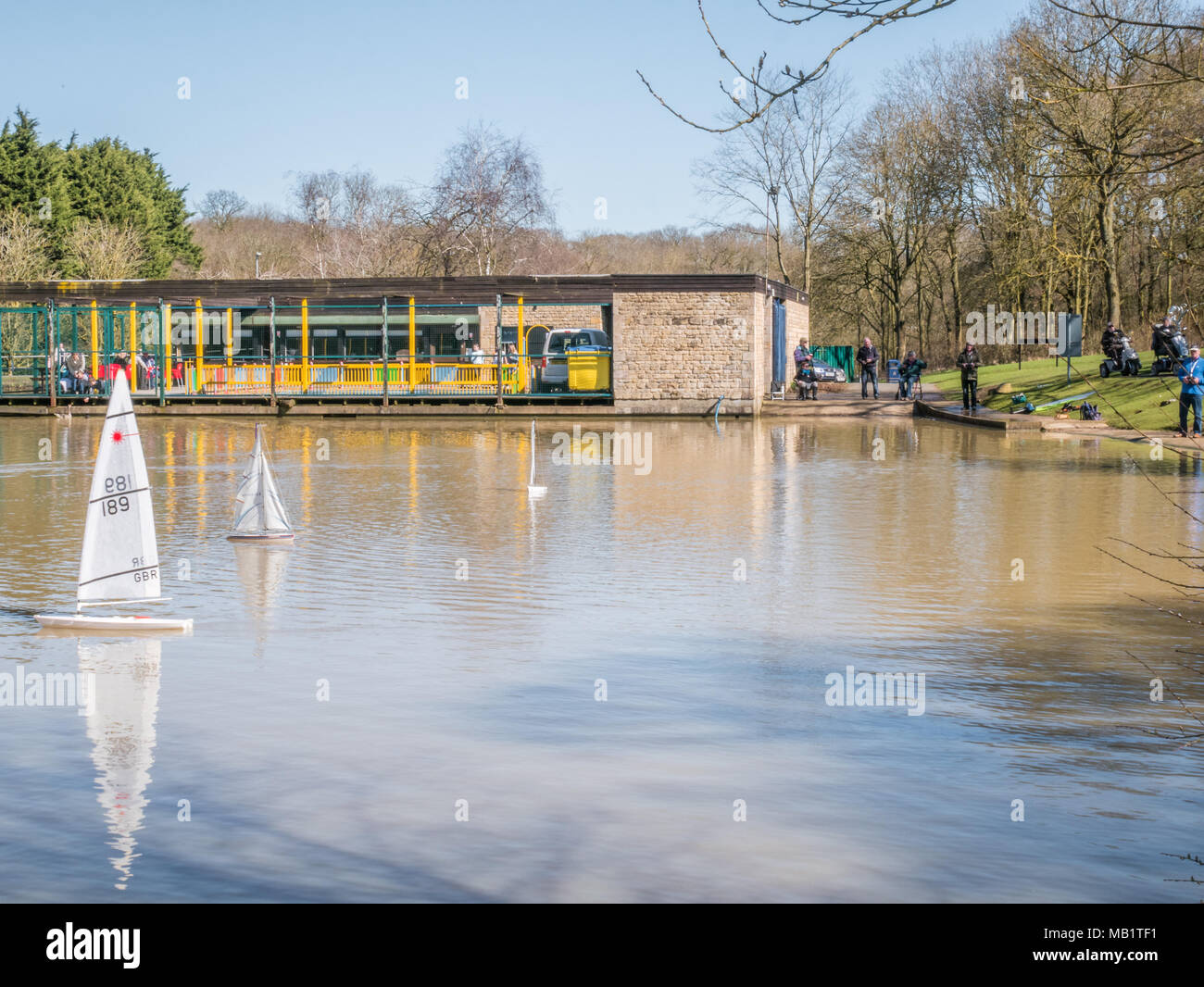 Männer nutzen Fernbedienungen ihr Spielzeug sawialing Boote auf dem See neben dem Cafe in Corby, England zu steuern, im Frühling. Stockfoto