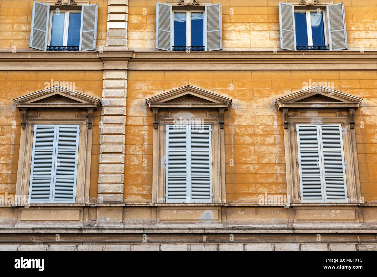 Blaue Fensterläden und verwitterten gelb gestrichenen Wänden auf einem Gebäude in der Stadt Rom, Italien. Stockfoto