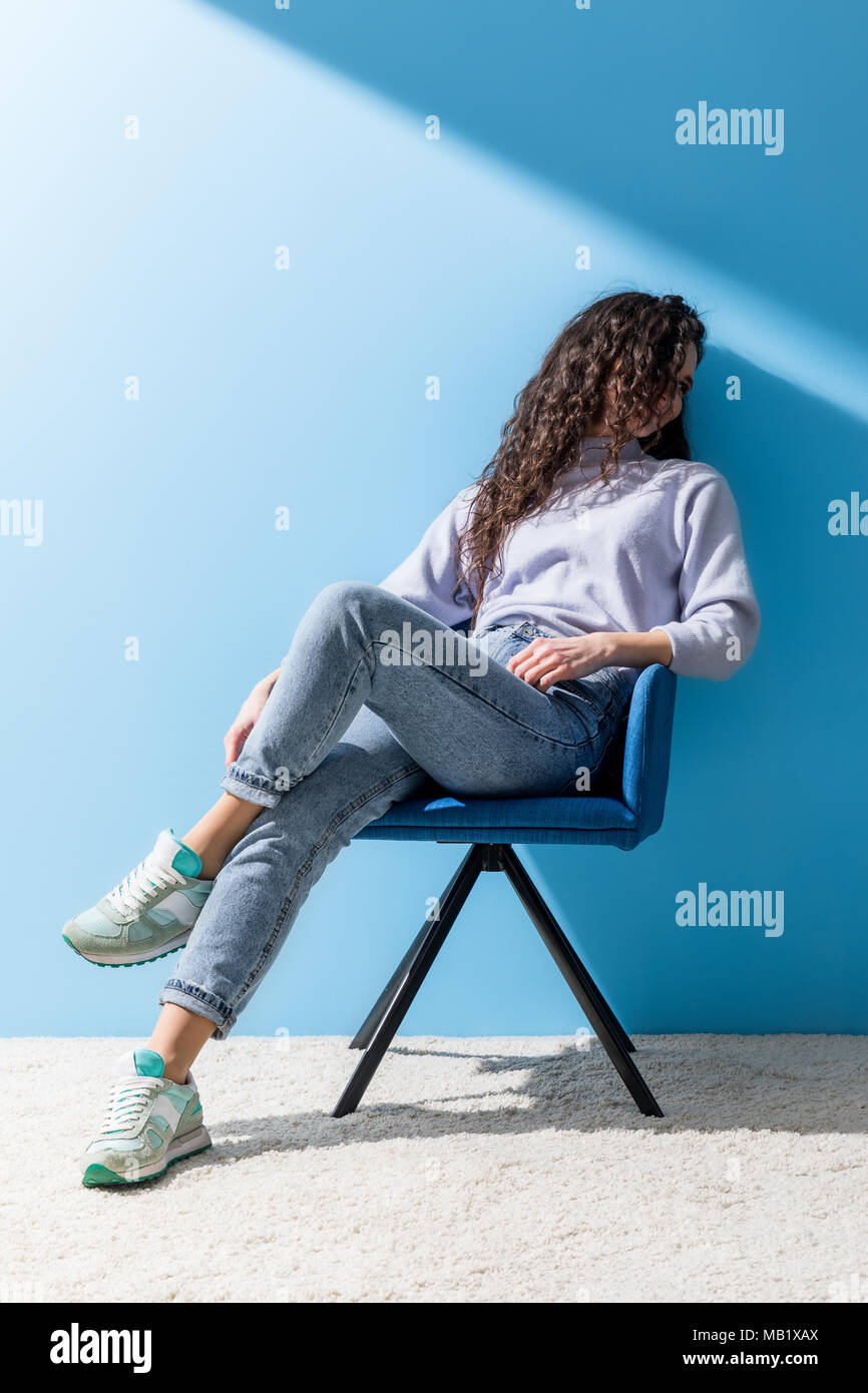 Attraktive junge Frau im Sessel vor der blauen Wand saß Stockfoto