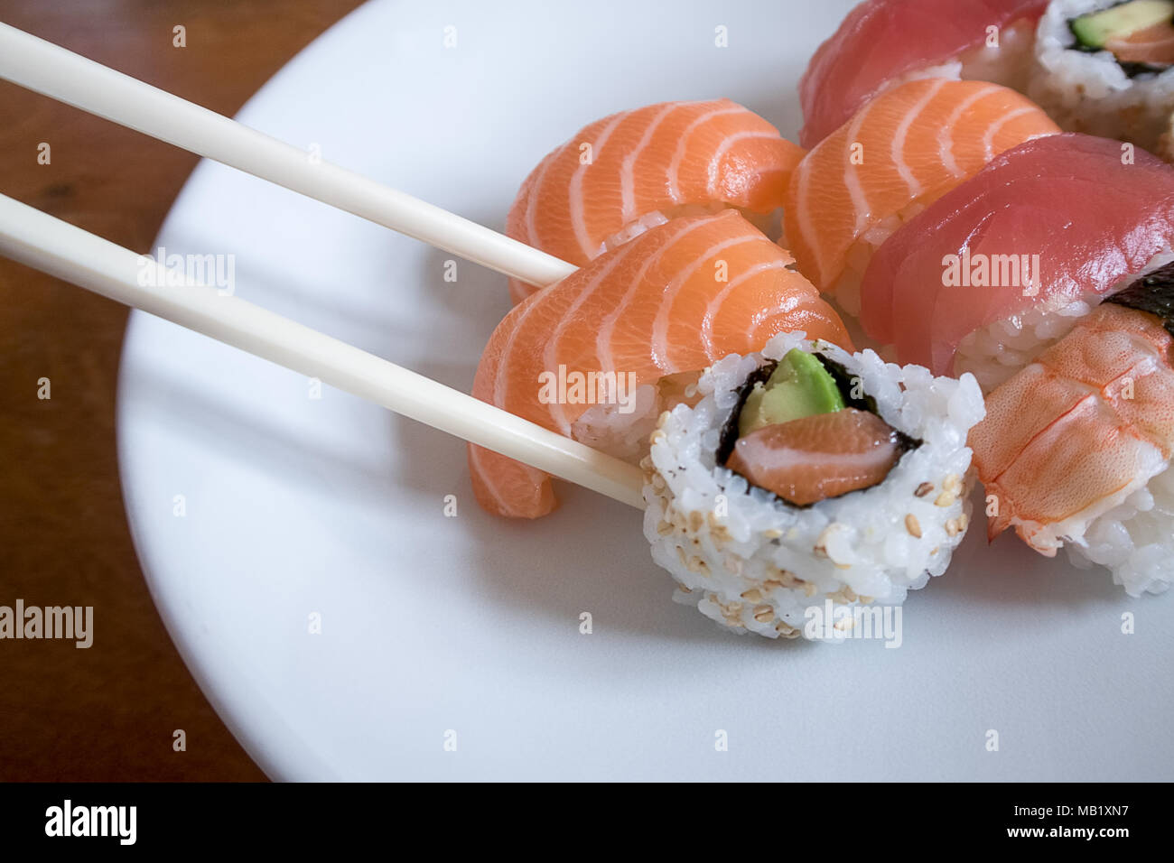 Frischer Lachs nigiri Sushi zwischen Stäbchen zusammen mit Uramaki, Garnelen Nigiri und Thunfisch nigiri Stockfoto