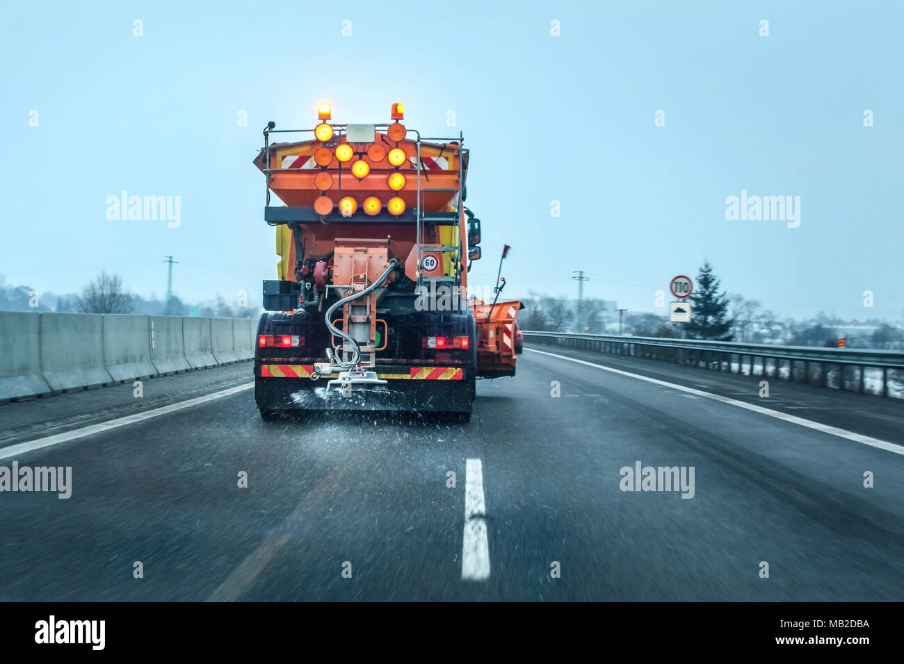 Blick aus dem Auto hinter Orange highway Maintenance truck Verbreitung Streusalz und Sand, kristalle fallen auf dem Eis bedeckten Asphalt. Stockfoto