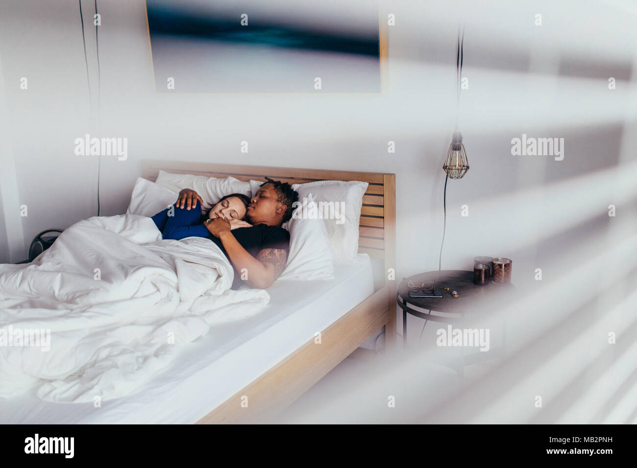 Interracial junges Paar umarmen während des Schlafens auf dem Bett. Mann und Frau schlafen friedlich im Schlafzimmer. Stockfoto