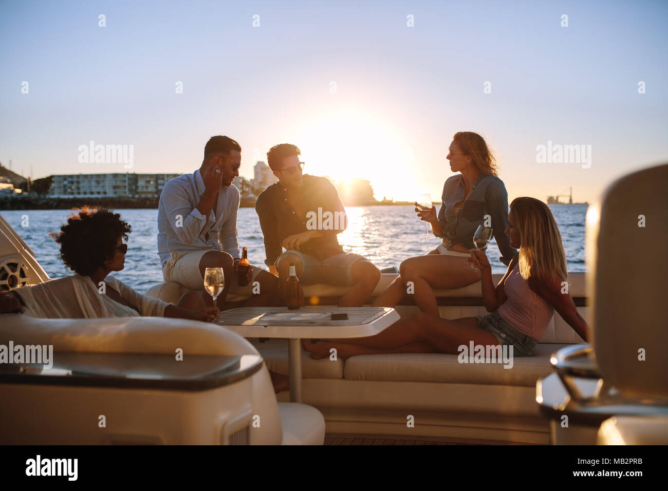 Junge reiche Freunde trinken Wein und Bier in Boot Partei während des Sonnenuntergangs. Gruppe von Jugendlichen feiern auf der Yacht. Stockfoto
