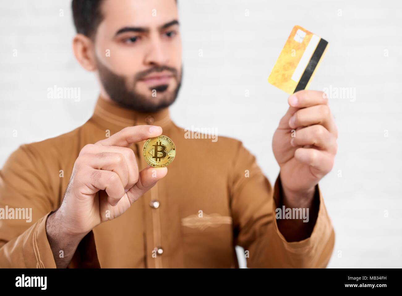 Arabische Geschäftsmann golden Bitcoin hält in der einen Hand und goldene Kreditkarte in einem anderen. Er trägt beige Shirt mit einem Muster. Close-up Studio war auf dem weißen Hintergrund. Stockfoto
