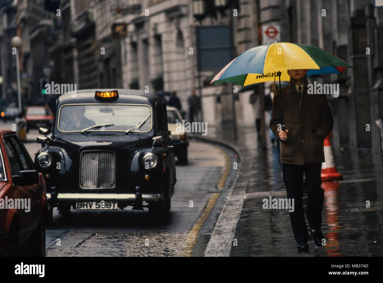 Stadt London England UK Heavy Rain und Taxi mit amn und Regenschirm 1985  Stockfotografie - Alamy