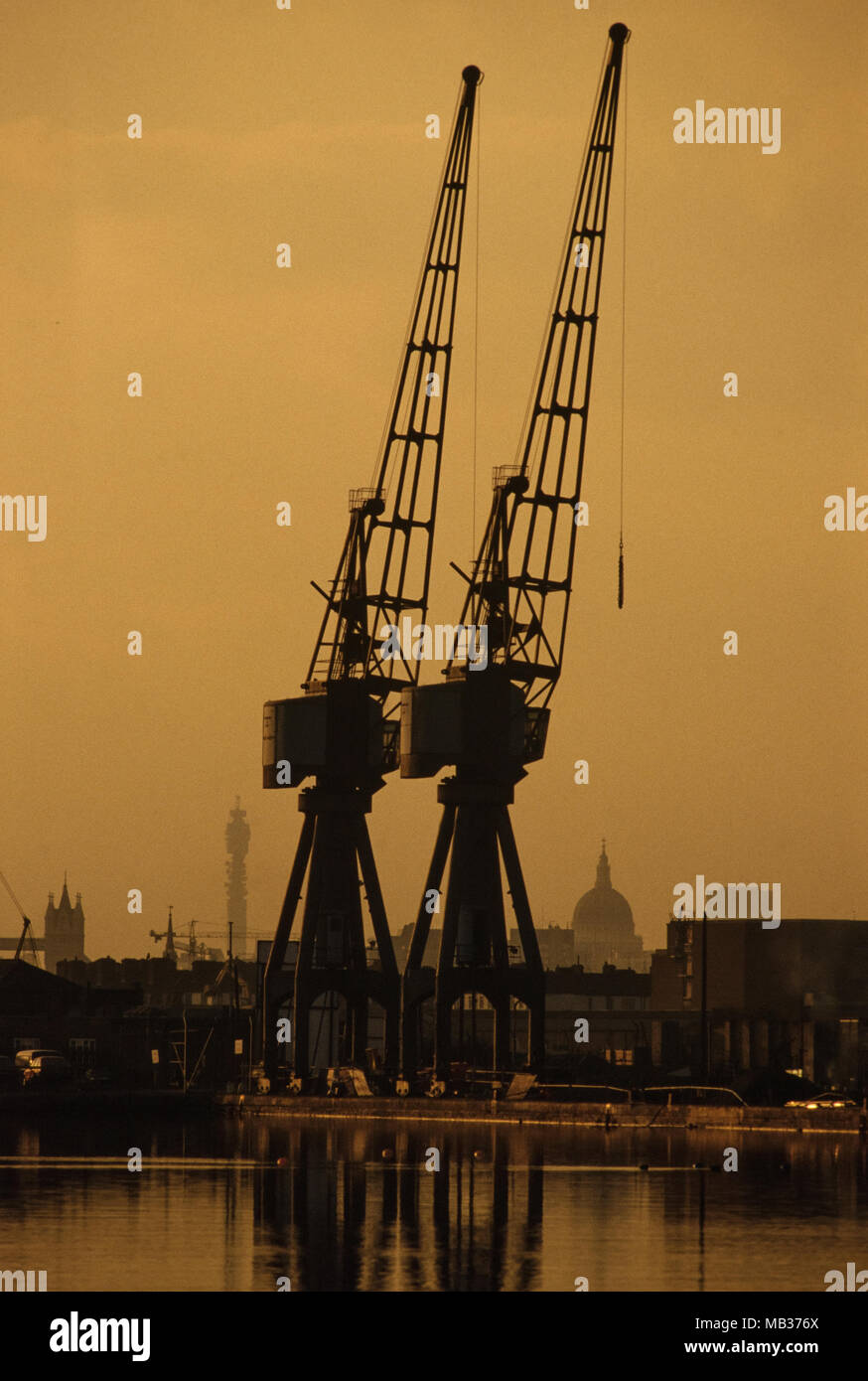 Isle of Dogs Docklands in London zeigen, Kräne und St Pauls Cathedral und der Post Tower in der Abenddämmerung. 1990 Stockfoto