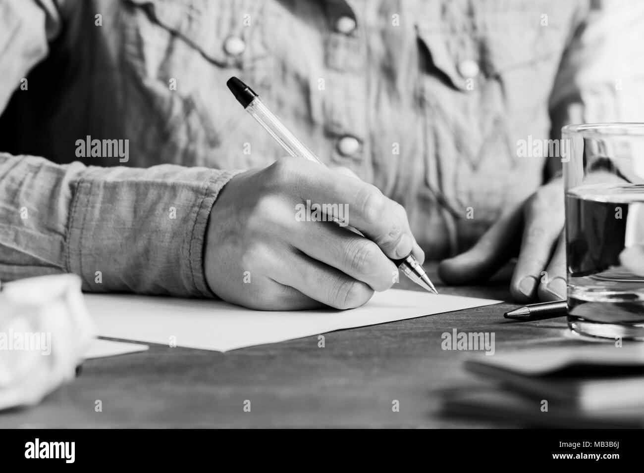 Der Mann ist schriftlich auf einem weißen Blatt Papier an einem Arbeitsplatz. Das Konzept von Arbeit und Bildung. Die Schwarz-Weiß-Fotografie. Stockfoto
