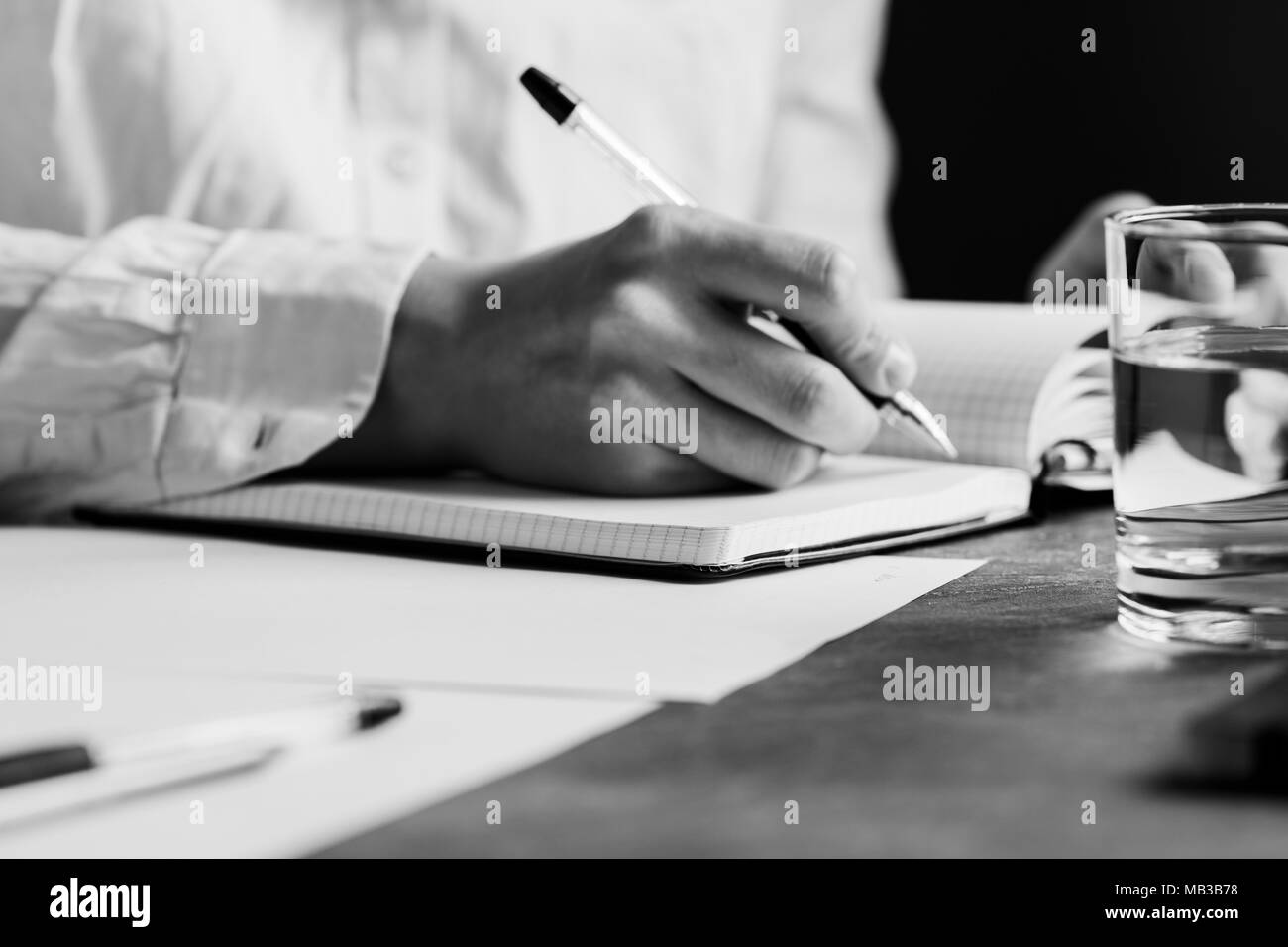 Der Mann ist schriftlich in einem Notebook an einem Arbeitsplatz. Das Konzept von Arbeit und Bildung. Die Schwarz-Weiß-Fotografie. Stockfoto