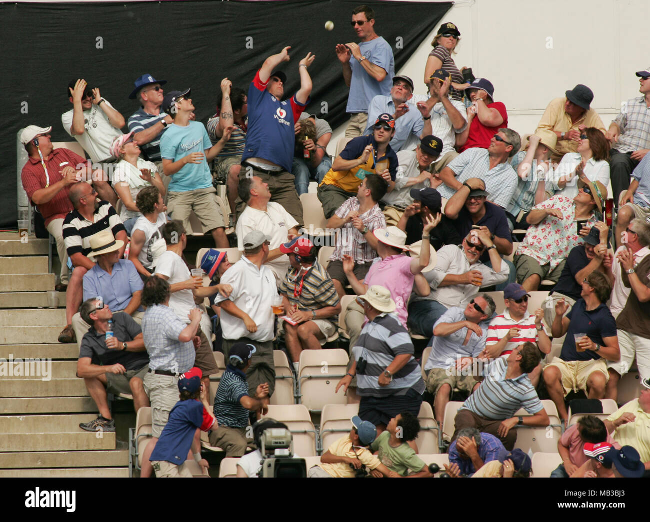 Eine Grille Kugel geht in die Menge während eines Cricket Match und es wird versucht, durch einen Ventilator, während andere Fans Ente erwischt zu werden und Dodge den ankommenden Ball. Stockfoto