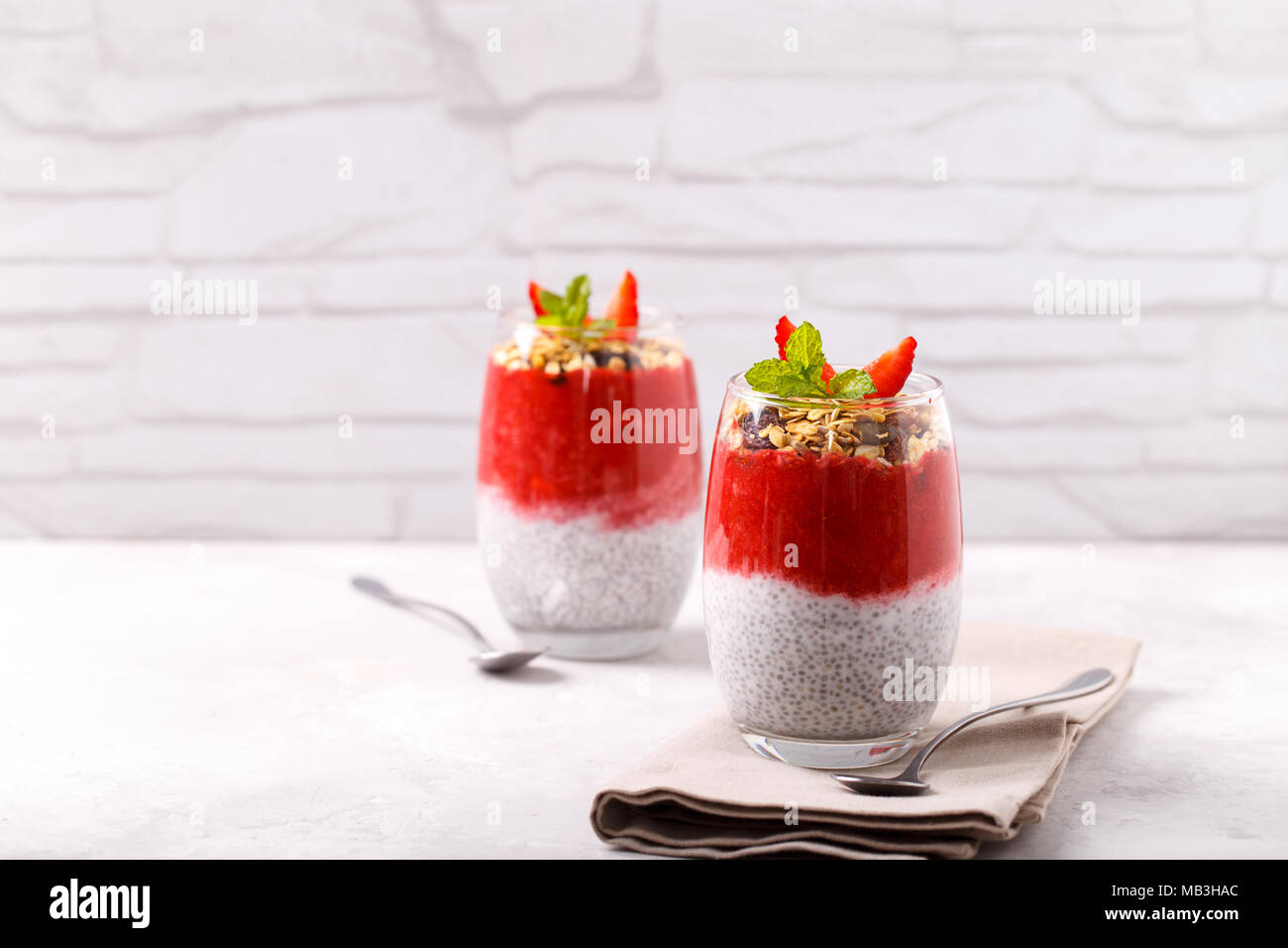 Gesunde Chia, Kokos, Erdbeere Pudding mit hausgemachtem Müsli auf weissem Holztisch Stockfoto