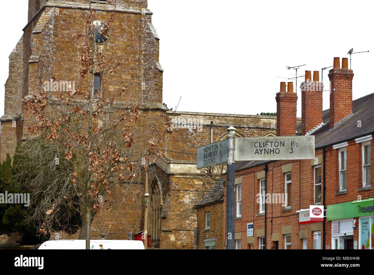 Deddington Stadtzentrum, Oxfordshire, UK, schmutzige Schild für Hemton, Banbury, Oxford, Clifton und Ayho sowie Deddington Kirche mit Uhr Stockfoto