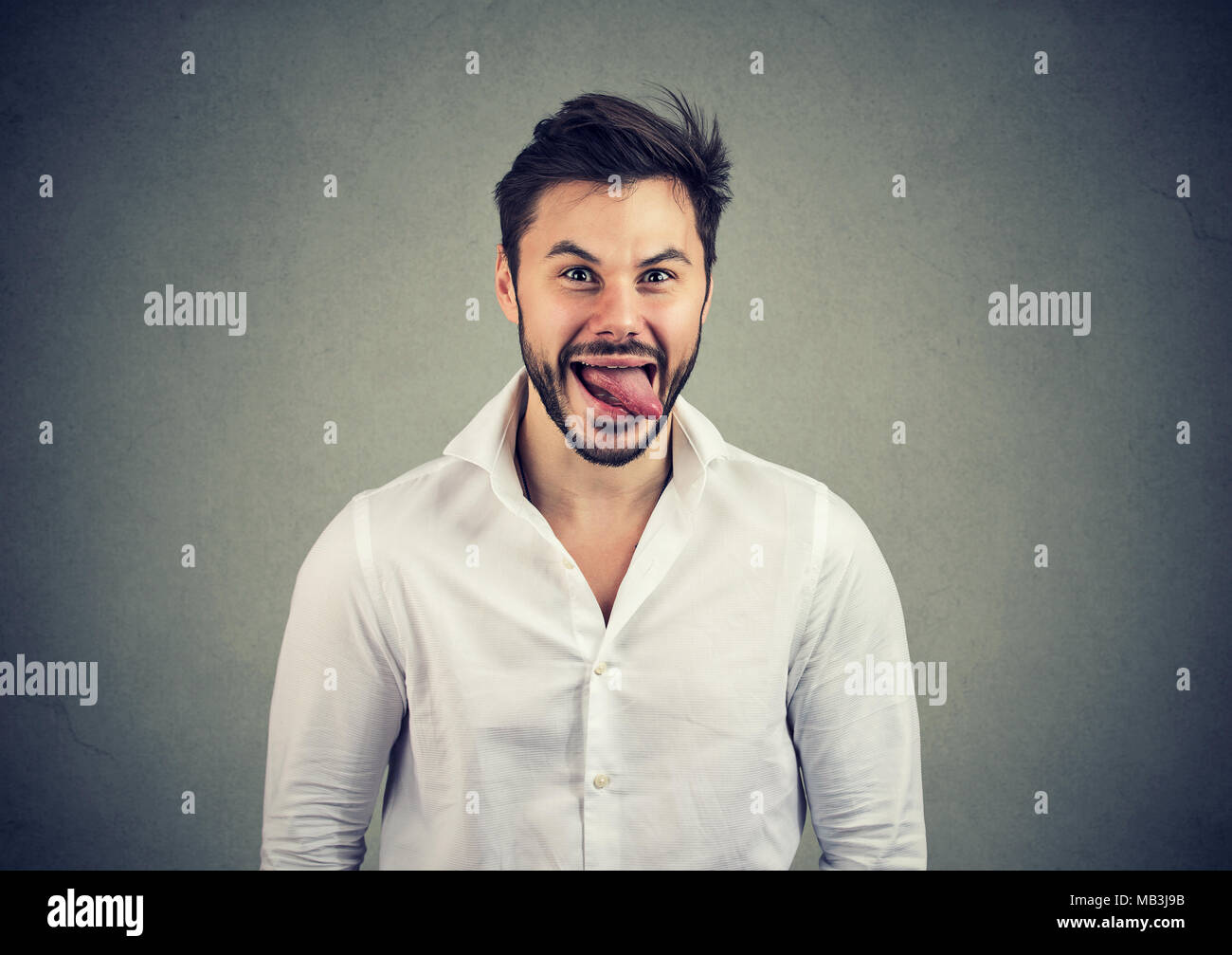 Junge legerer Mann im weißen Hemd, Gesicht und Zunge an Kamera und Witz. Stockfoto