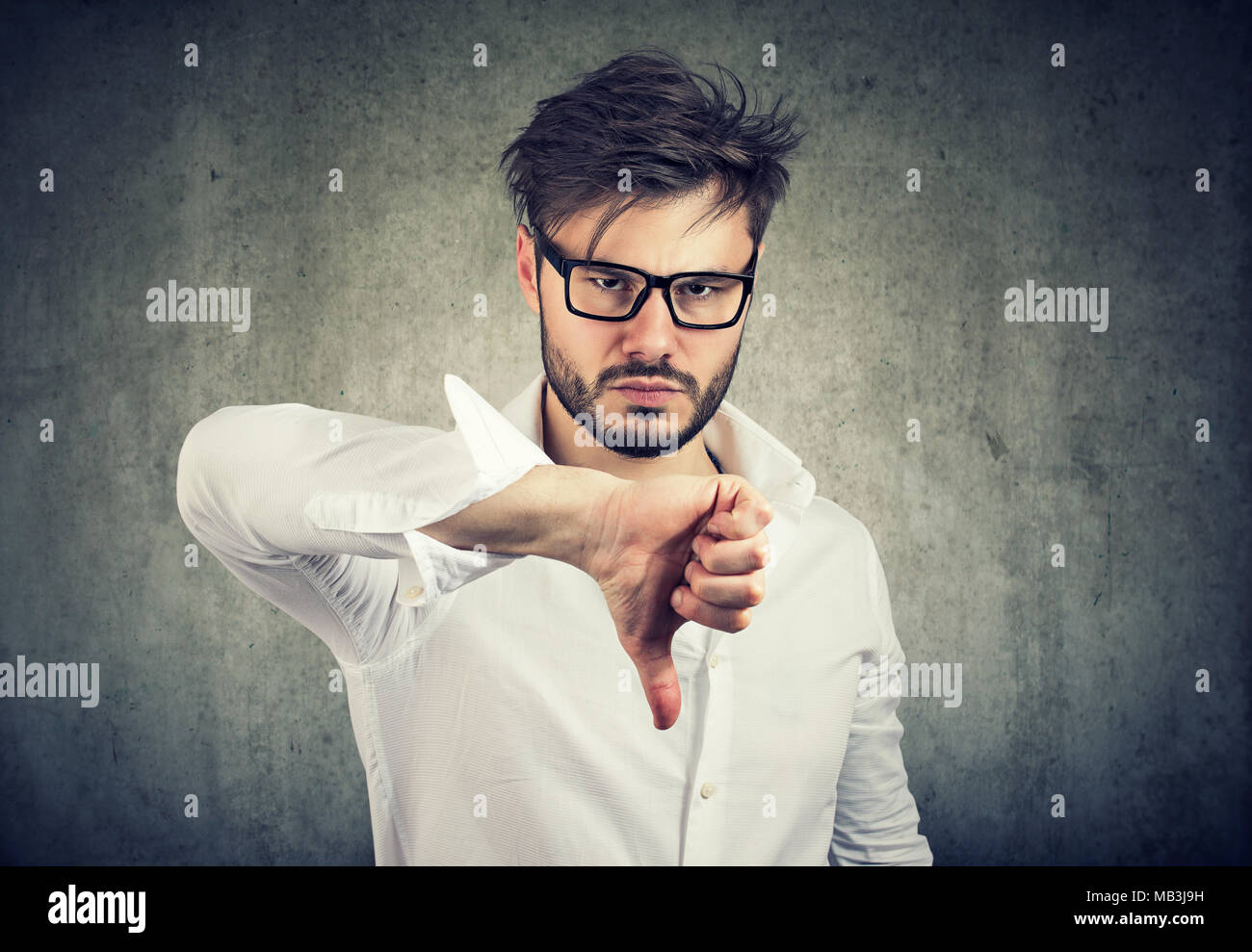 Stirnrunzelnd Mann in Brillen holding Daumen nach unten an der Kamera in Abneigung. Stockfoto