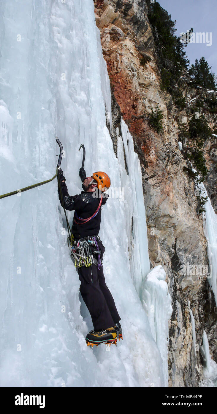 Männliche Eiskletterer auf einem steilen gefrorenen Wasserfall an einem schönen Wintertag in den Schweizer Alpen Stockfoto