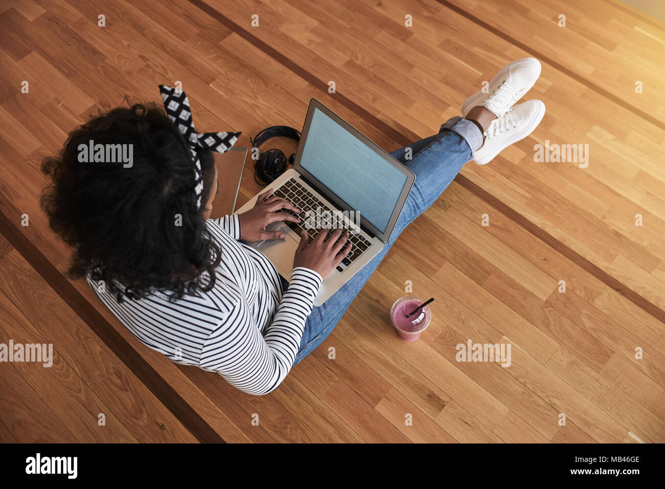 Hohen Winkel eines afrikanischen Studenten online arbeiten mit einem Laptop beim Sitzen auf dem Boden in einem campus Flur zwischen Klassen Trinken einer smo Stockfoto