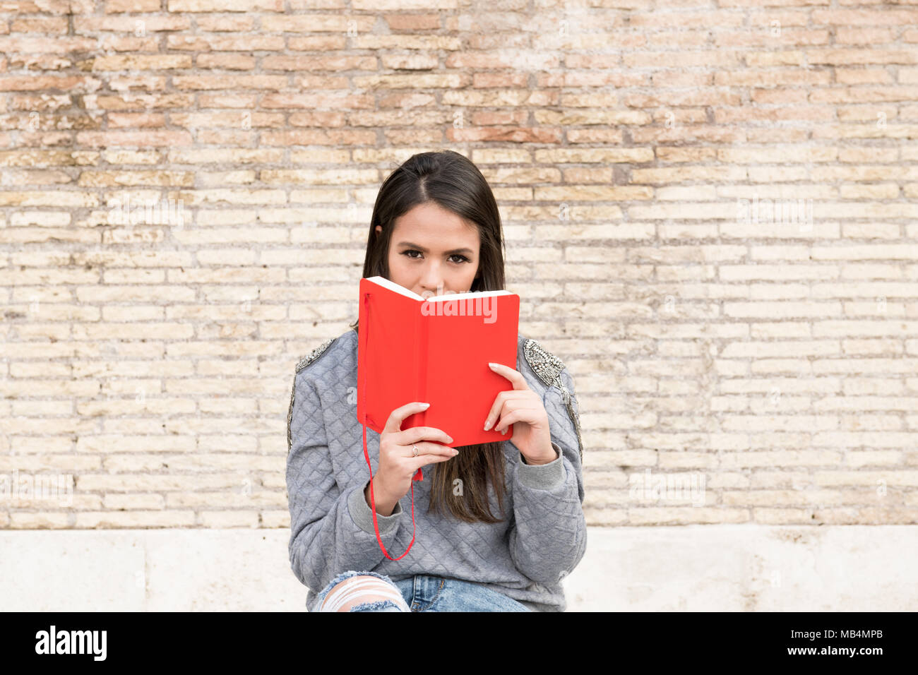 Junge latina Frau sitzt auf der alten Marmorbank Platz im Freien, mit roten Buch in den Händen zu kopieren Stockfoto