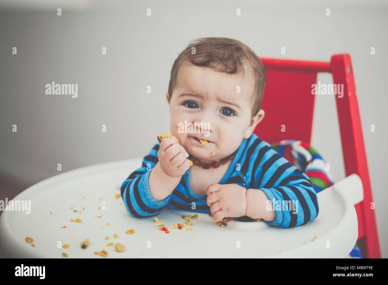 6 Monate alten Baby Junge selbst Fütterung in einem Hochstuhl Stockfoto