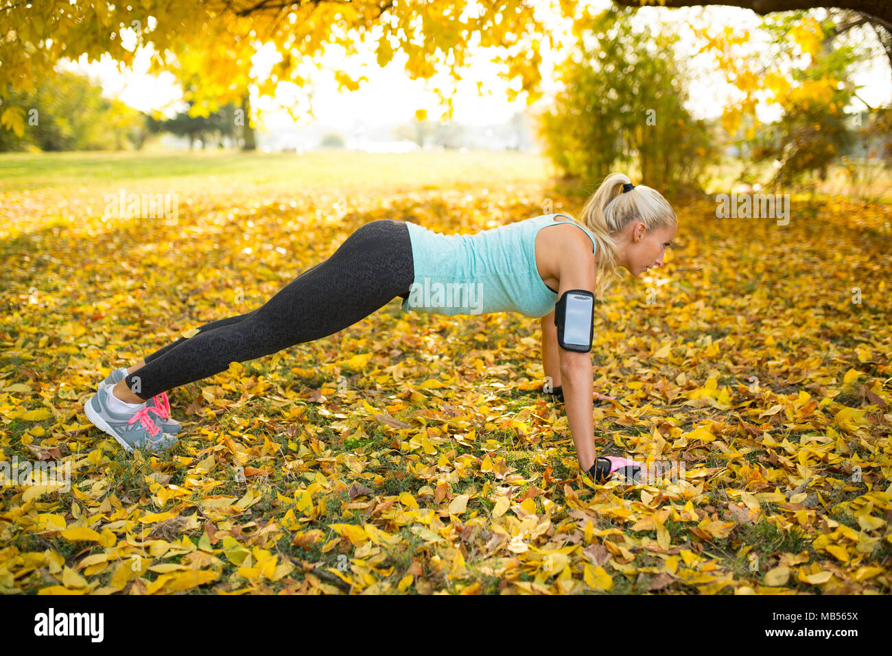 Attraktive blonde Frau tun Push-ups in den öffentlichen Park mit Blättern bedeckt. Stockfoto