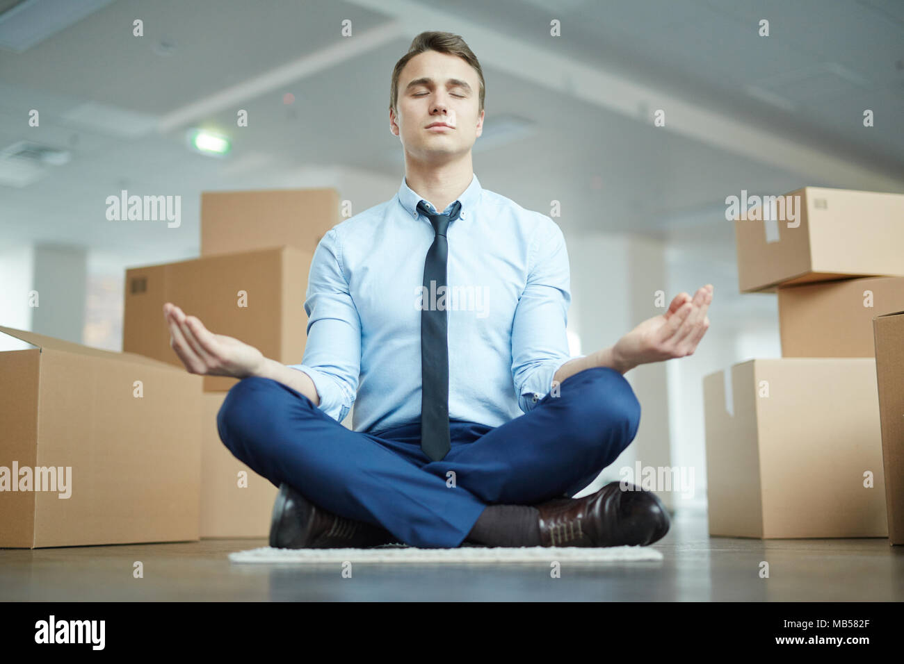 Junge Manager in formale sitzen auf dem Boden in der Pose des Lotus und Meditieren nach stressigen Tag im neuen Büro Stockfoto