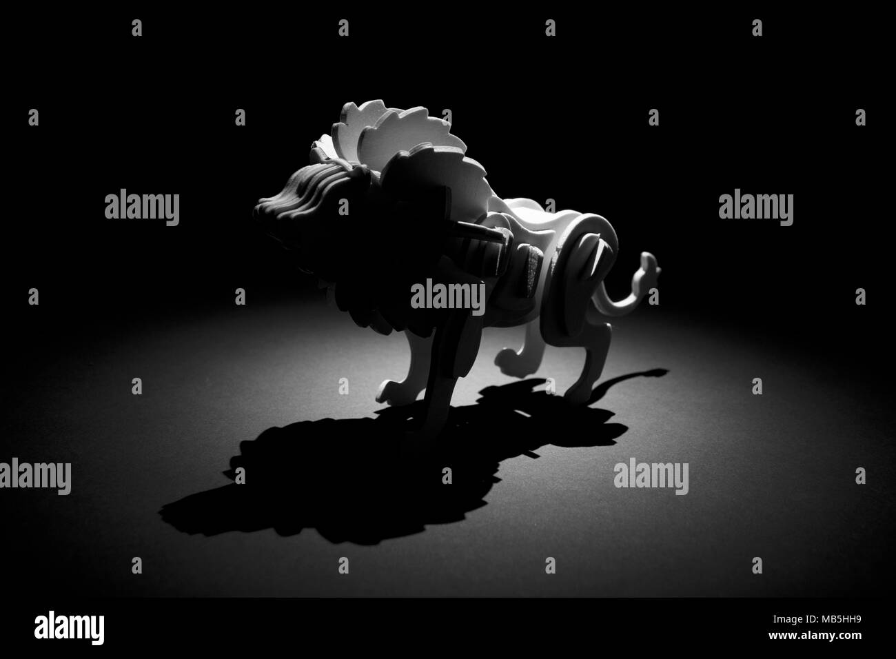 Stilisiertes Löwenmodell, von hinten beleuchtet, wirft einen dramatischen Schatten gegen einen schwarzen Hintergrund Stockfoto