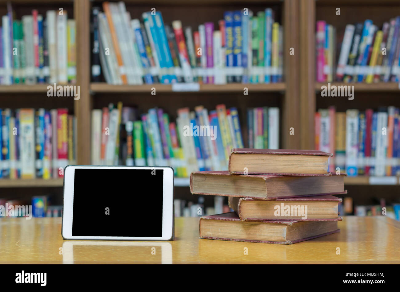 Altes Buch auf dem Schreibtisch in der Bibliothek mit Tablet Stockfoto