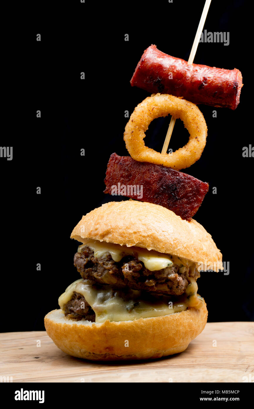 Eine doppelte Wildschwein Burger aus einem Wildschwein geschossen in der Toskana, Italien, mit cambozola Käse und mit Chorizo Wurst und frittierten Zwiebeln garniert r Stockfoto