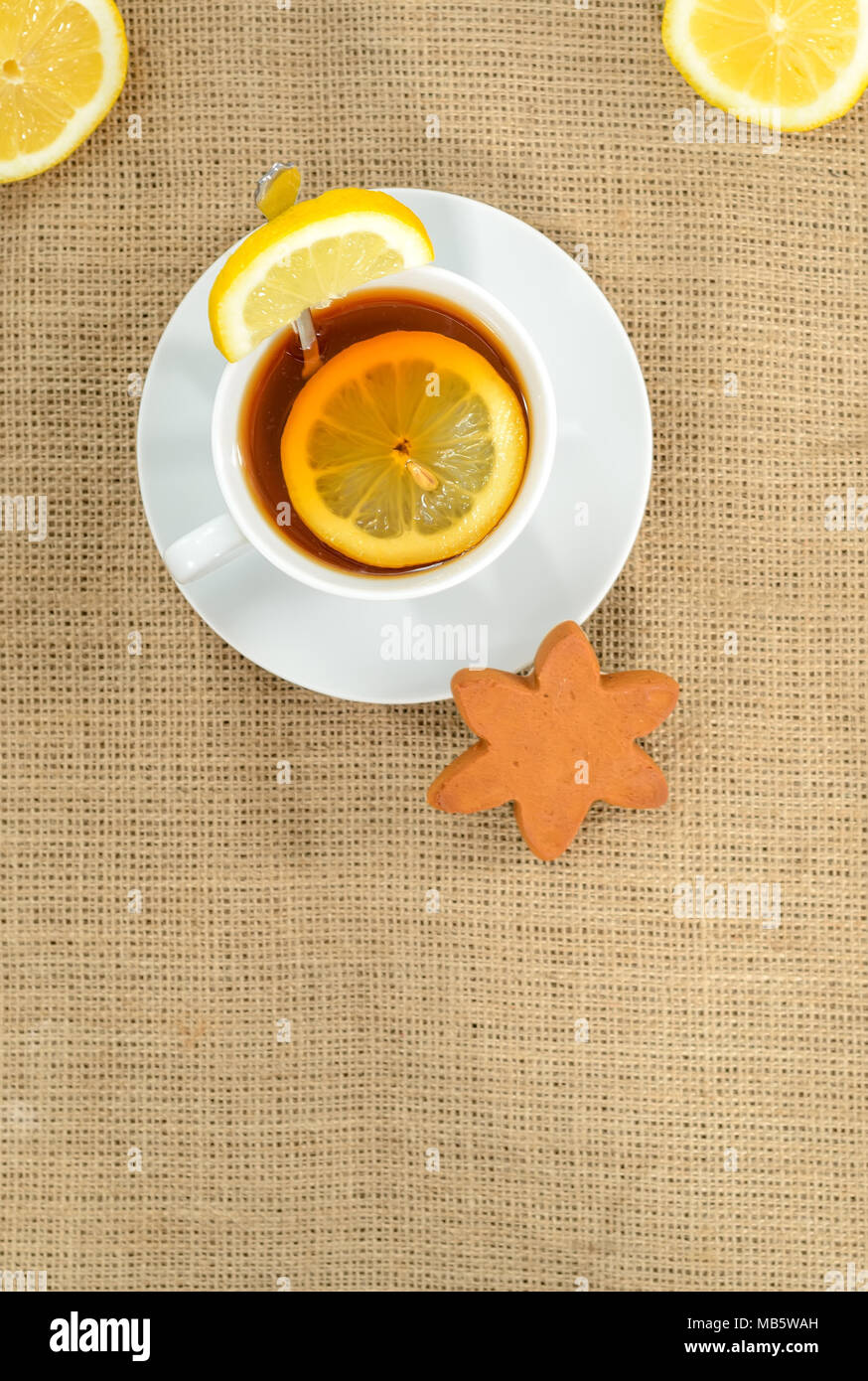 Eine Tasse Tee mit Zitrone und ein zwei halbe Zitronen in jeder Ecke und ein Stern Cookies auf sackleinen Hintergrund. Hochformat. Raum nach unten. Stockfoto