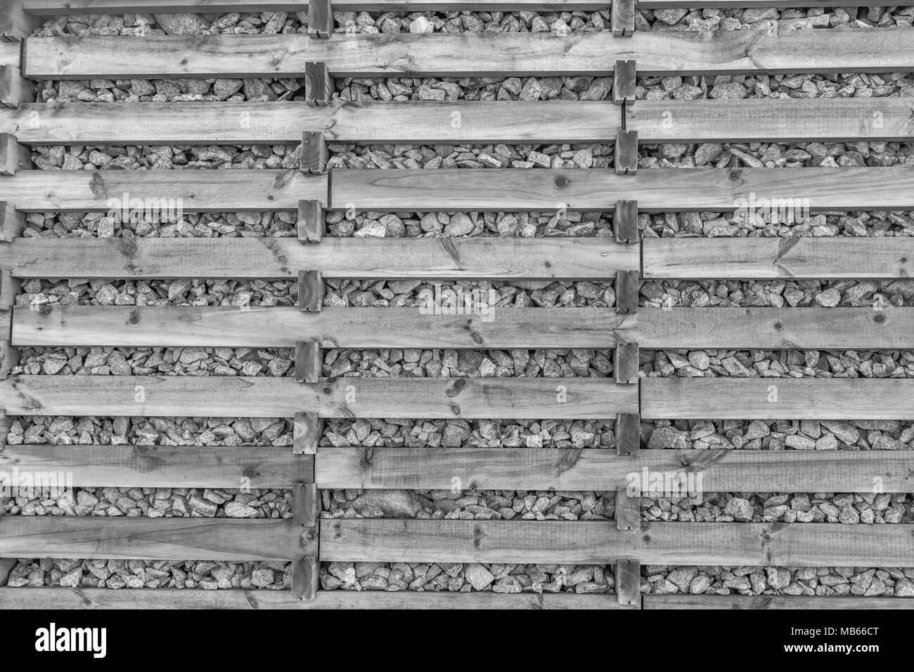 Schwarz-weißes abstraktes Bild von Steinen, die von Holzschlitzkonstruktion oder -Rahmen zurückgehalten werden. Holz und Steine Hintergrund. Stockfoto