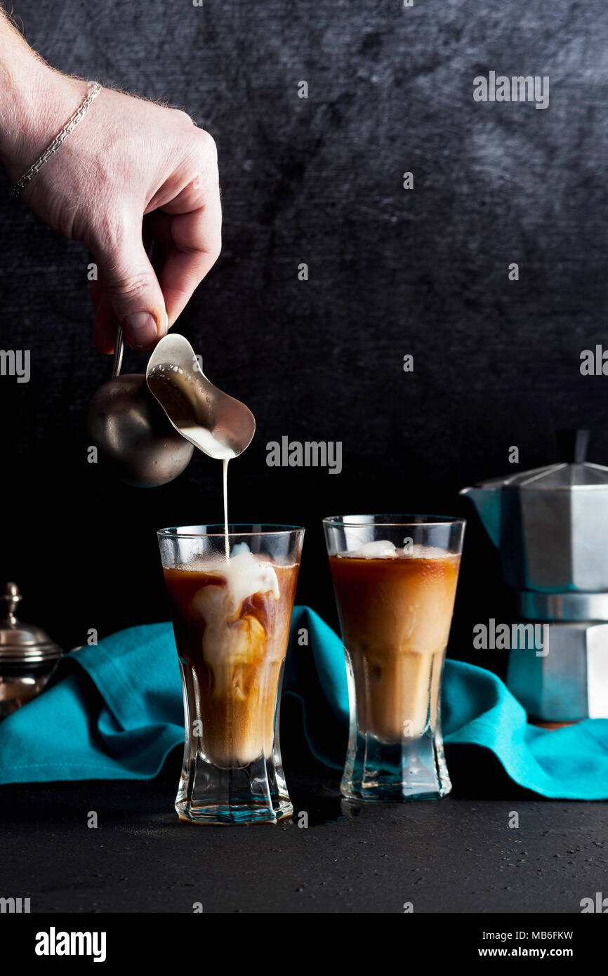 Die Hand des Mannes gießt Milch auf Eiskaffee, schöne und saubere Komposition. Kaffeemaschine an zurück Stockfoto