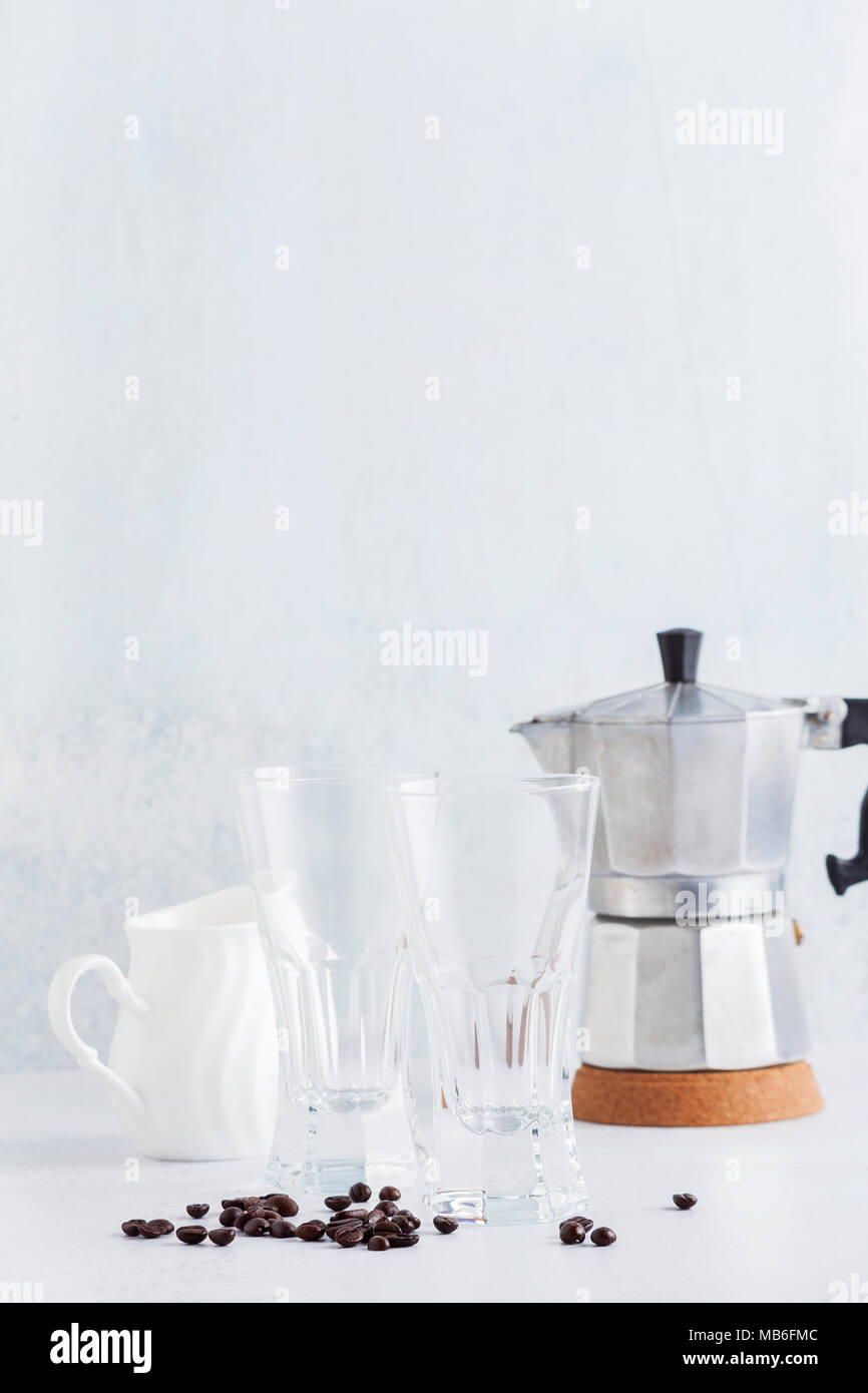 Leere Gläser und ein Milchkännchen mit Kaffeebohnen und eine Kaffeemaschine auf dem Tisch. Stockfoto