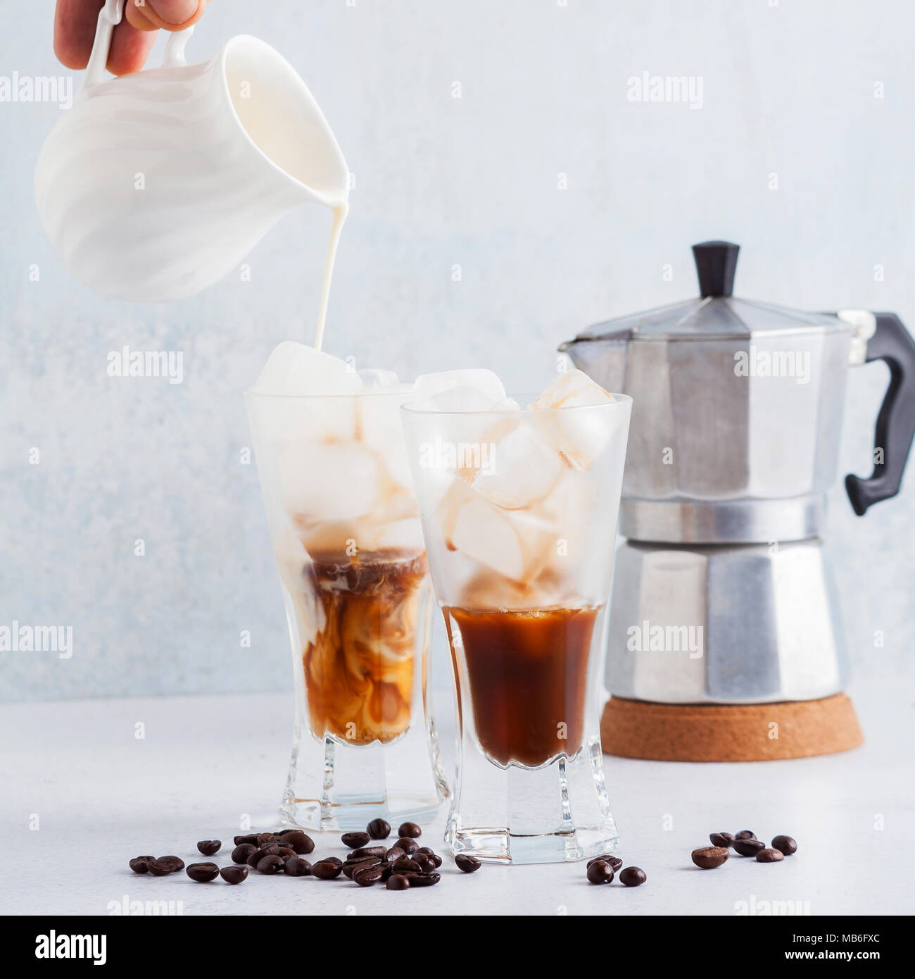 Die Hand des Mannes gießt Milch auf Eiskaffee, schöne und saubere Komposition. Kaffeemaschine an zurück Stockfoto